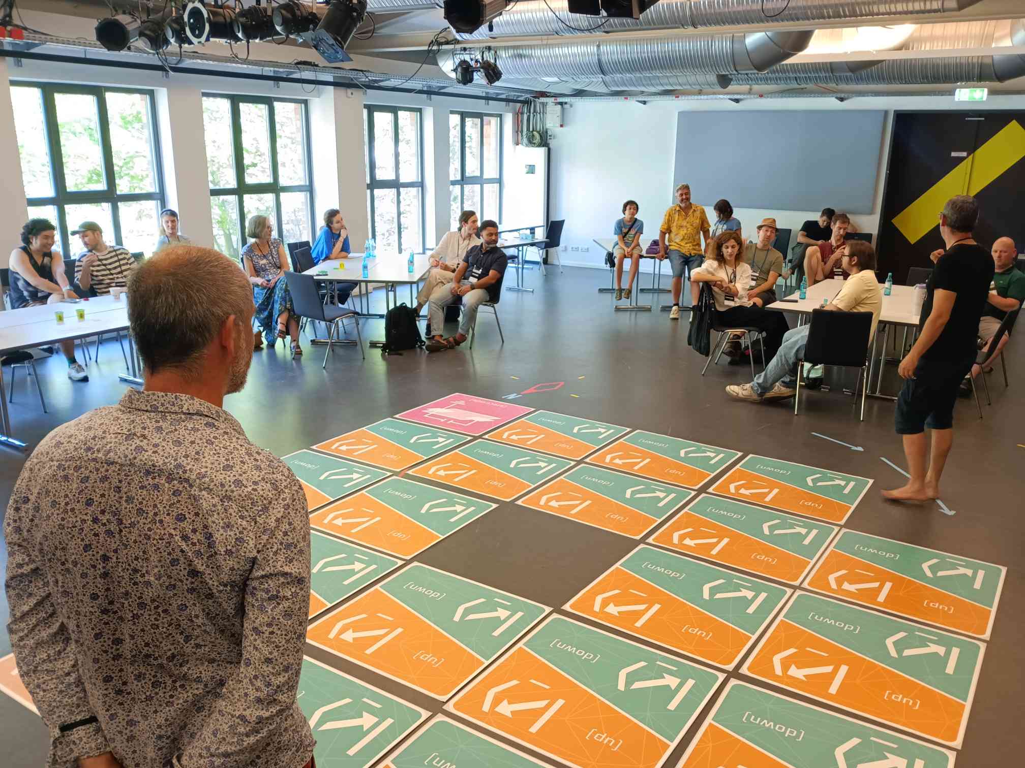 A facilitator watches a participant step across the |HOP⟩ grid while the room observes